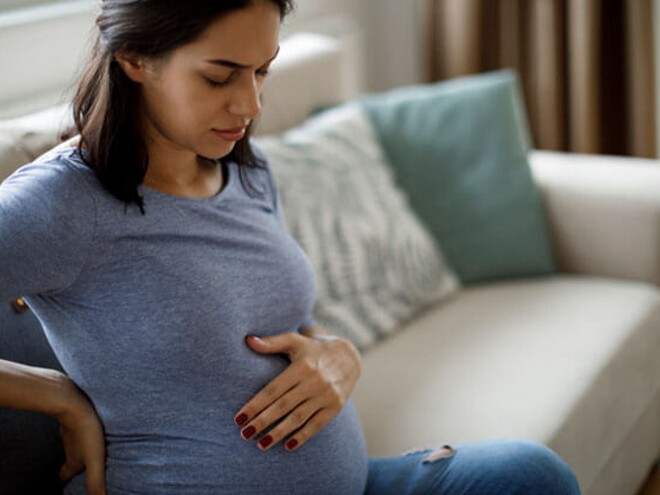 Mamá tocando el vientre y la espalda sintiendo molestia.