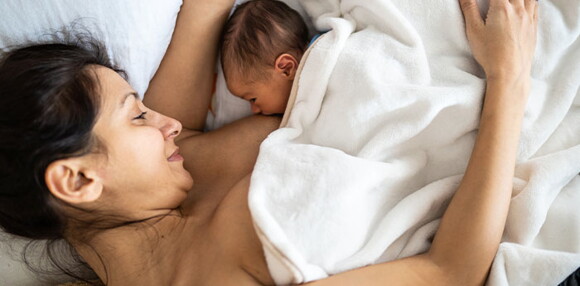 Mamá acostada alimentando a su bebé recién nacido.