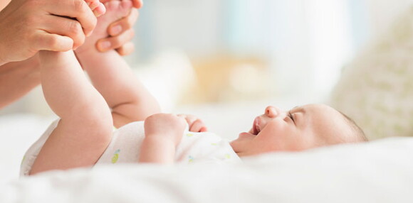 Bebé de dos meses sonriendo con las piernas levantadas.