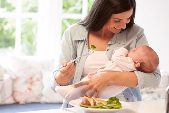 Una madre comiendo con su bebé en brazos