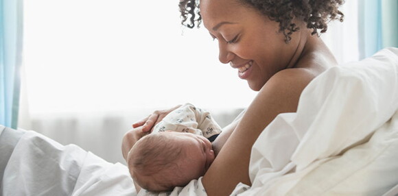 Mamá acostada alimentando a su bebé recién nacido en la cama.